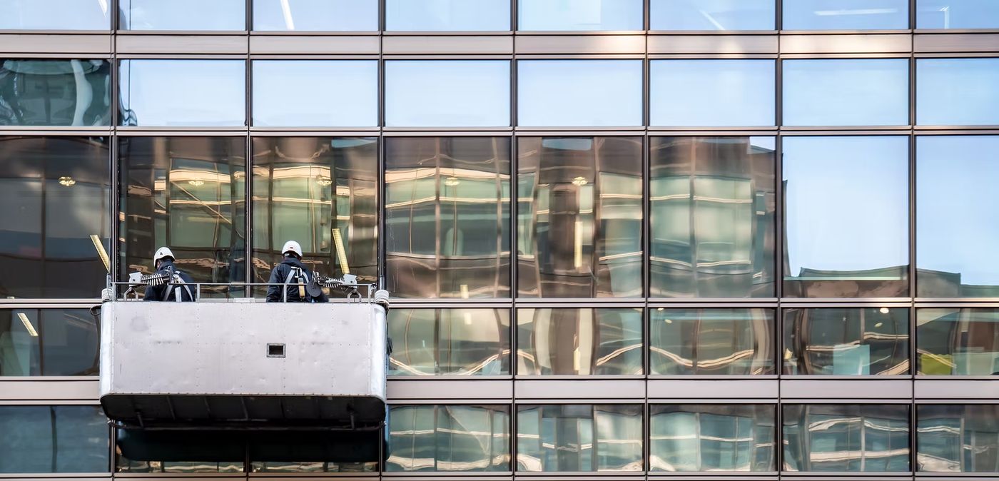 Two technicians on gondola lift cleaning glass building facade