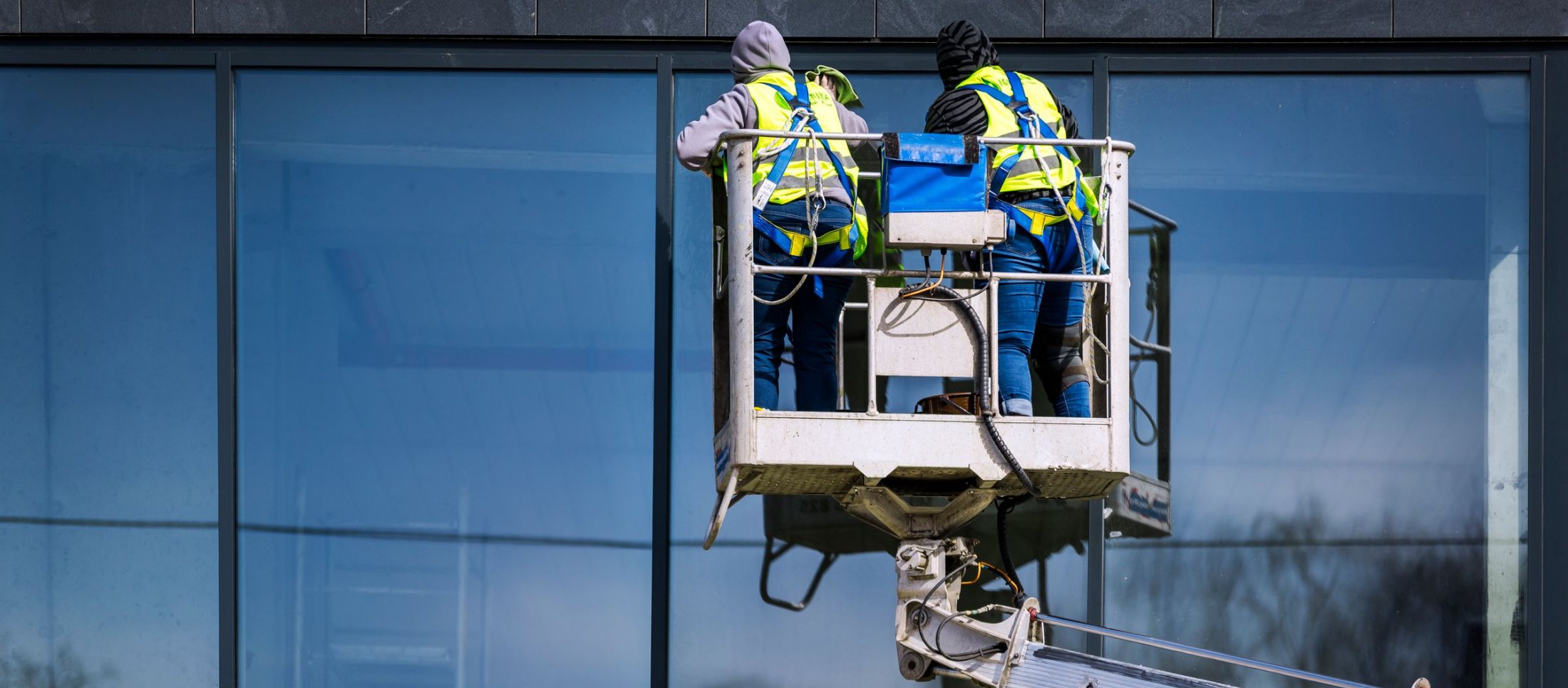 Two window cleaners in safety harnesses on a lift cleaning a glass office facade